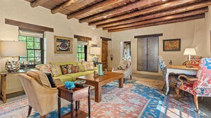 A spacious living room with a wooden ceiling, a green sofa, a coffee table, and a patterned rug. - Casa Verano | Cozy Eastside Adobe Retreat (Santa Fe)