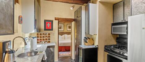 A compact kitchen with granite countertops, a stainless steel sink, a stove, and a microwave.