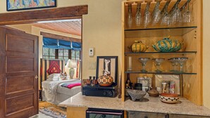 A kitchen with a wooden door, a countertop with a coffee maker, and a shelf with glassware. - Casa Verano | Cozy Eastside Adobe Retreat (Santa Fe)