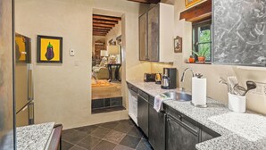 A kitchen with granite countertops, a sink, and a window with a plant. - Casa Verano | Cozy Eastside Adobe Retreat (Santa Fe)