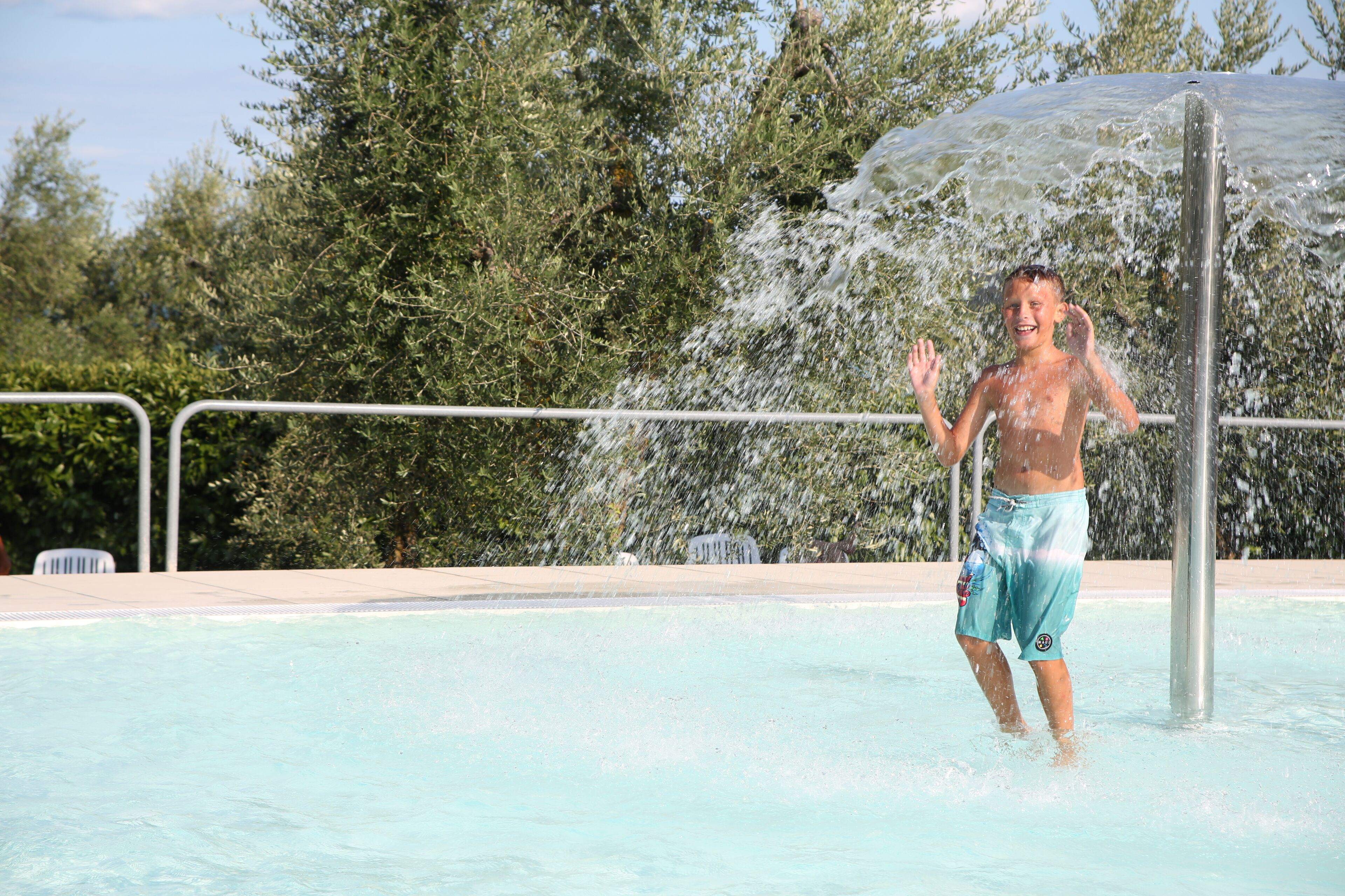 A person in a swimming pool with water spraying from a fountain.