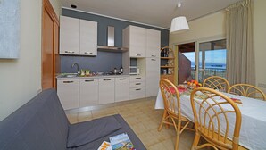 Cocina compacta con armarios blancos, zona de comedor con mesa y sillas, y balcón con vistas.