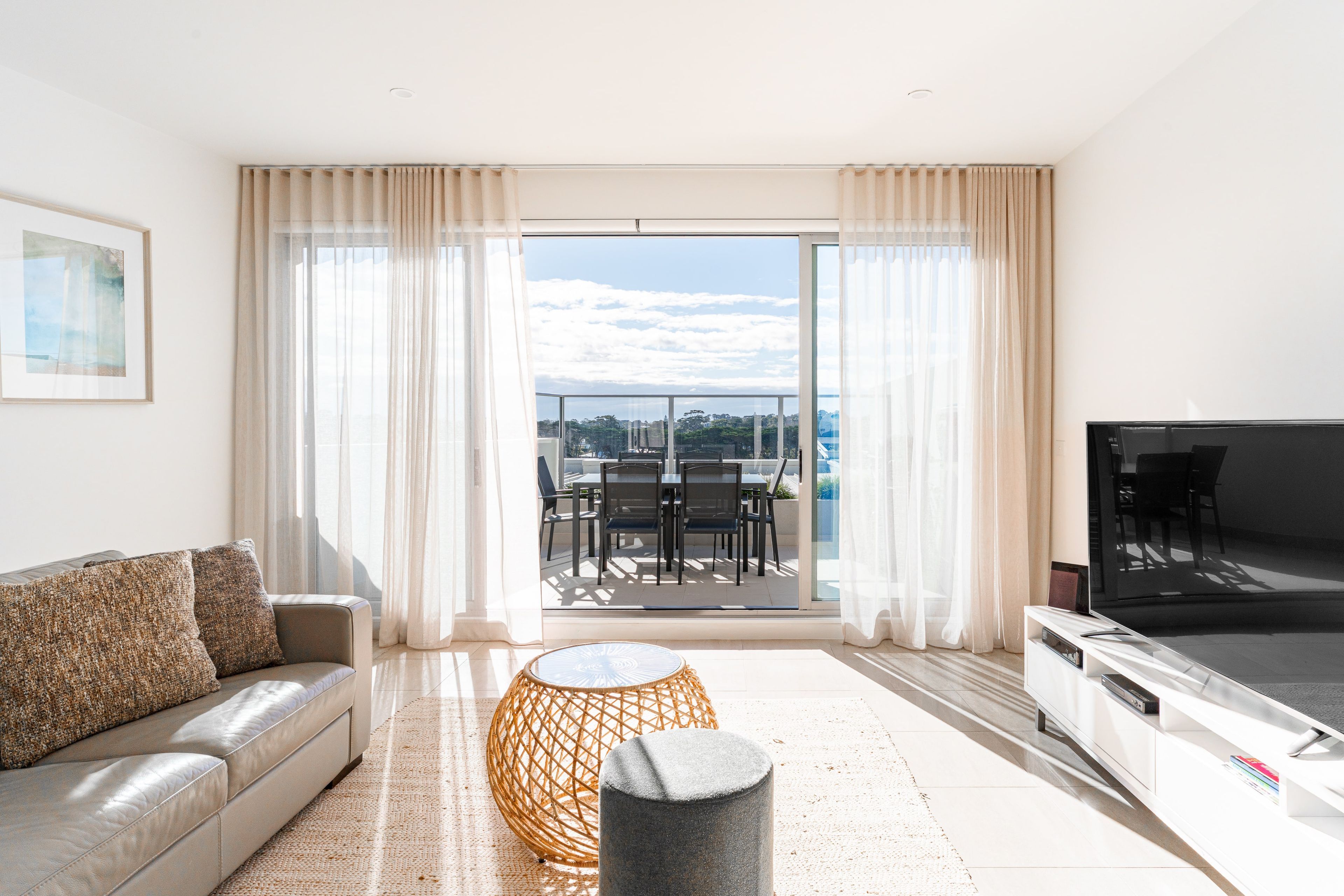 A modern living room with a sofa, a coffee table, a TV, and a balcony with outdoor furniture.