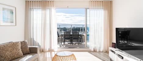 A modern living room with a sofa, a coffee table, a TV, and a balcony with outdoor furniture.