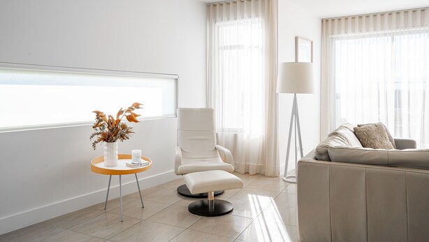 Un salon moderne avec un canapé blanc, un fauteuil, une lampe sur pied et une fenêtre ornée de rideaux légers.