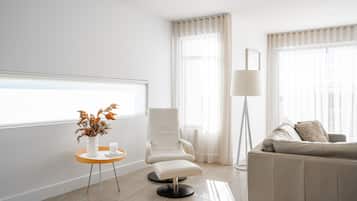 A modern living room with a white sofa, a chair, a floor lamp, a small table with a vase, and a window with sheer curtains.