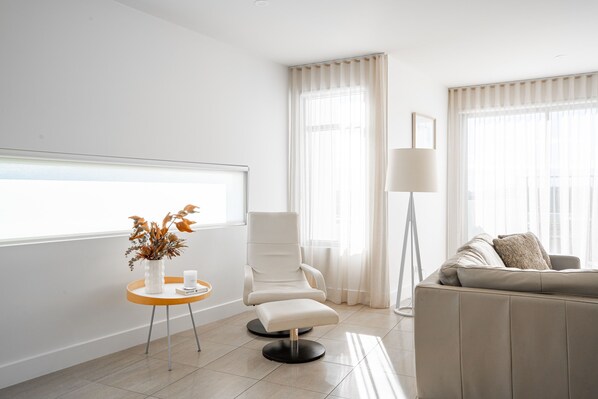 A modern living room with a white sofa, a chair, a floor lamp, and a window with sheer curtains.