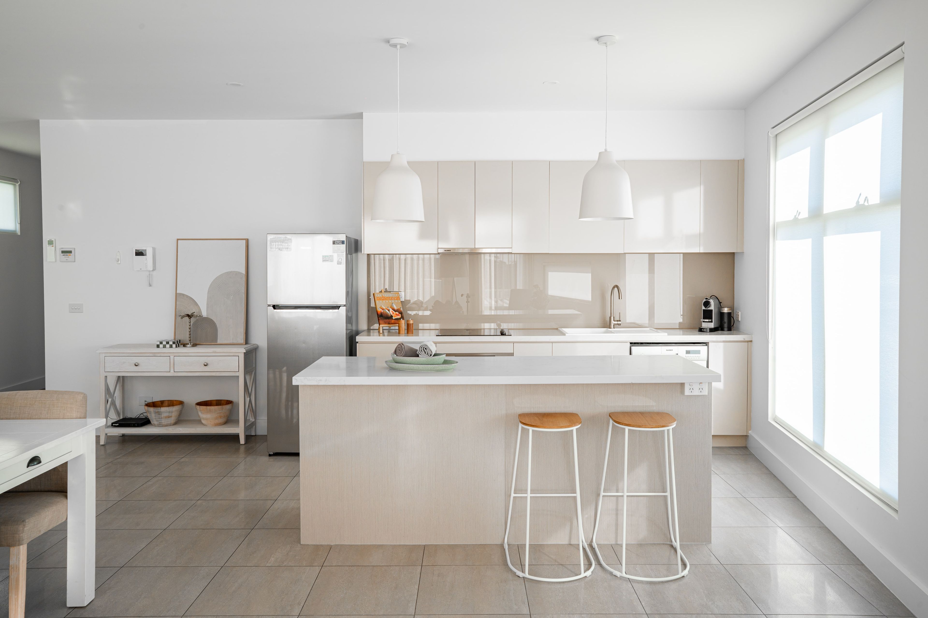 A modern kitchen with a central island, bar stools, and pendant lighting.