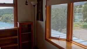 A room with a large window offering a view of a forested area and a building with a blue roof.