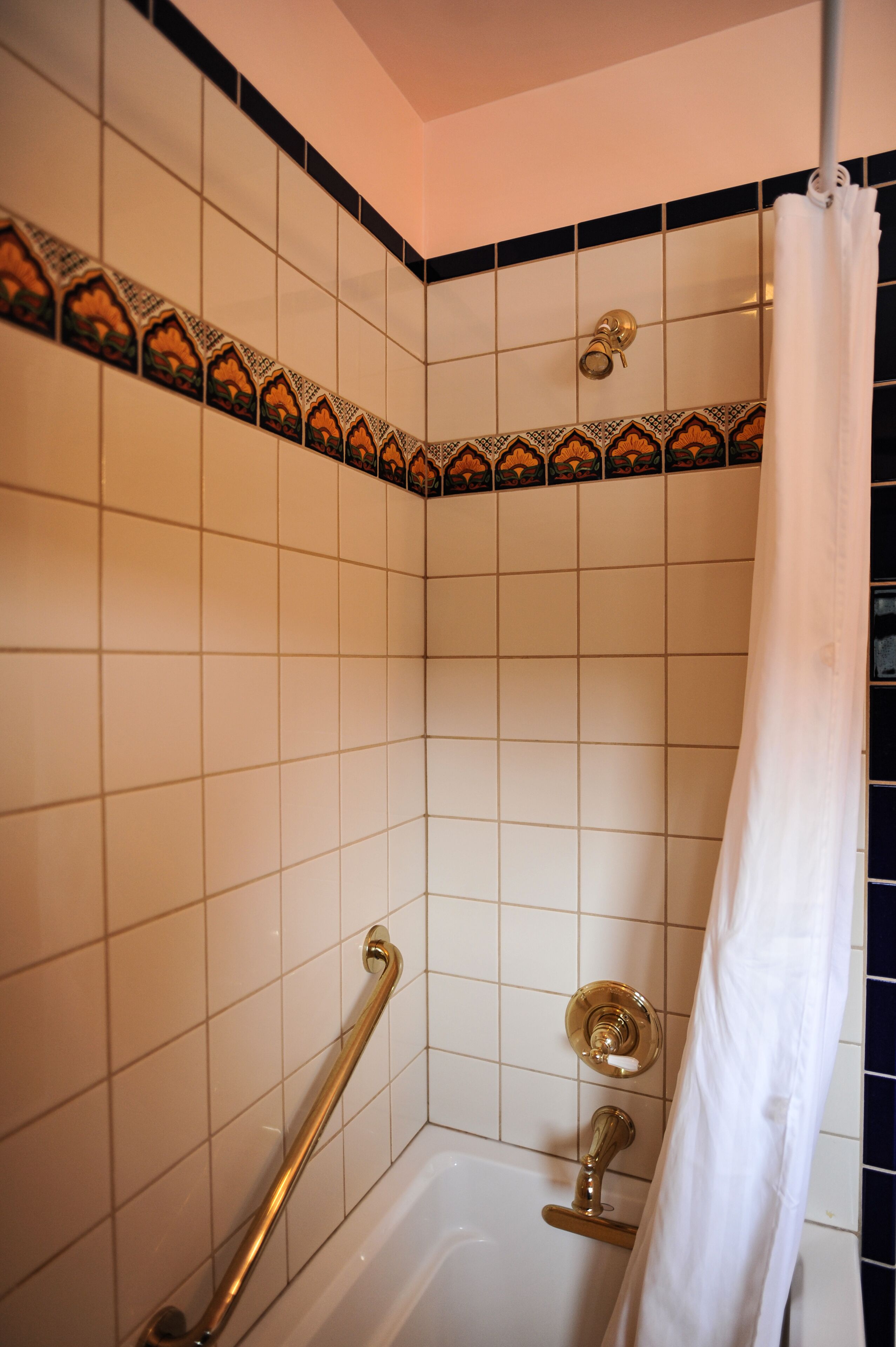 A bathroom with white tiles, a shower curtain, and a grab bar.