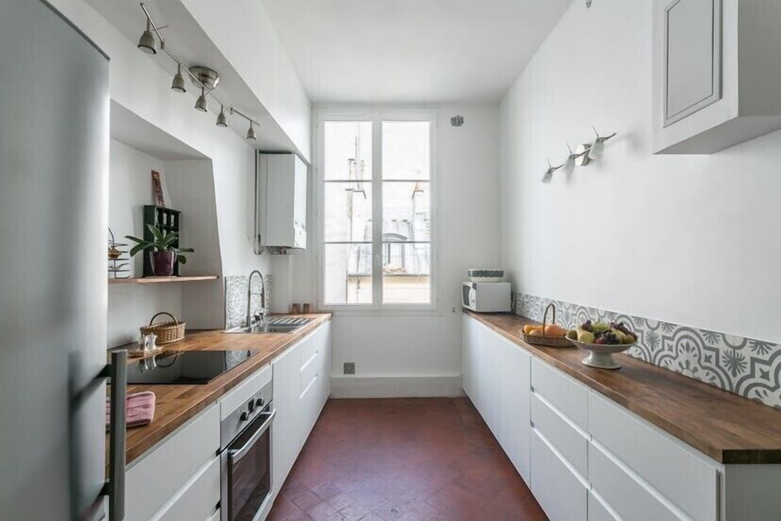 Una cocina estrecha con armarios blancos, una encimera de madera y una ventana.