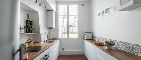 Una cocina estrecha con armarios blancos, una encimera de madera y una ventana.