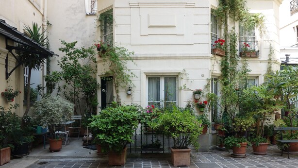 A courtyard with potted plants and a tiled floor, surrounded by buildings with balconies and windows. - Paris-sur-seine-chez-caroline (Paris)