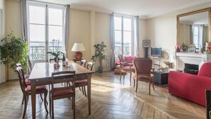 A spacious living room with a wooden herringbone floor, a dining area with a table and chairs, a red sofa, and a fireplace. - Paris-sur-seine-chez-caroline (Paris)