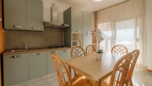 A modern kitchen with grey cabinets, a wooden dining table, and wicker chairs. - Three-room villa direct to the beach, 6 beds garden pool  (Manerba del Garda)