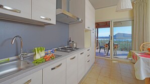 A modern kitchen with a sink, stove, and cabinets. There is a balcony with a table and chairs. - Three-room villa direct to the beach, 6 beds garden pool  (Manerba del Garda)