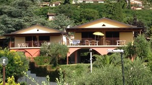 A two-story house with a balcony and a covered patio area. - Three-room villa direct to the beach, 6 beds garden pool  (Manerba del Garda)