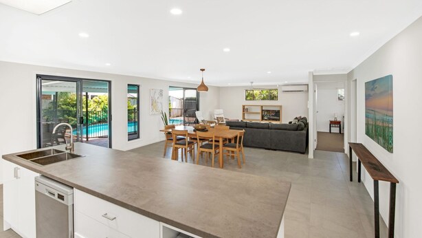 Una cocina moderna con una isla central, comedor y vista a una piscina.