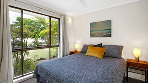 Un dormitorio con un ventanal grande, una cama con ropa de cama estampada, dos lámparas de noche y un cuadro en la pared.