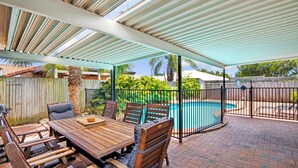 Un patio exterior con piscina, mobiliario de madera y una zona cubierta.