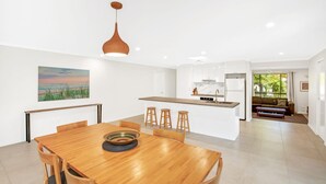 Una cocina moderna con armarios blancos, una isla de madera con taburetes y una lámpara colgante.