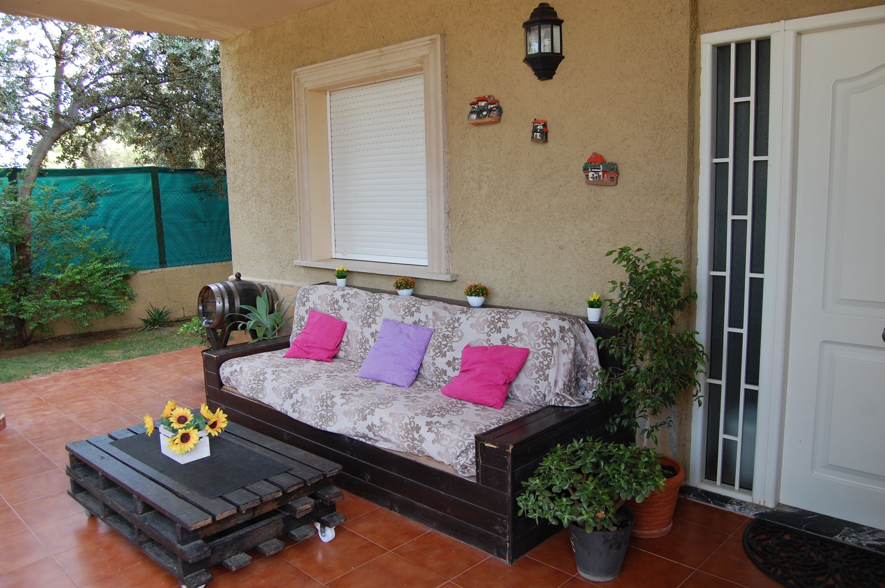 A patio area with a sofa, a small table with sunflowers, and potted plants.
