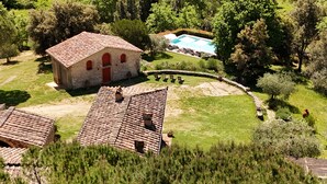 Un bâtiment de style rustique avec une porte rouge, entouré d’une pelouse bien entretenue et d’une piscine.