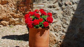 Un bâtiment rustique en pierre, avec un panneau portant le chiffre « 8 », une fenêtre ornée de fleurs rouges et un pot de fleurs rouges placé devant l’entrée.