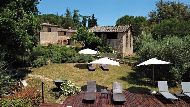 Un espace piscine agrémenté de chaises longues et de parasols, entouré d’une terrasse en bois et d’un jardin.
