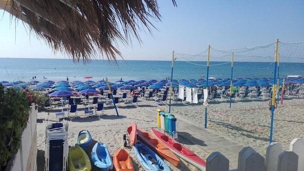 Ein Strand mit Reihen von Sonnenschirmen und Liegestühlen, und mehrere Boote am Ufer liegend.