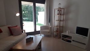 A living room with a sofa, a coffee table, a white armchair, a TV stand, and a bookshelf. - 2 Bedrooms, Beach at 300m, Parking (Albufeira)