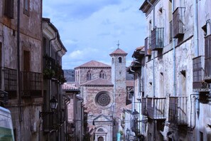 Une rue étroite bordée de bâtiments historiques, une église dotée d’une grande fenêtre circulaire et d’un clocher.