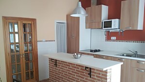 Una cocina compacta con una isla de ladrillo, armarios de madera, microondas y un lavamanos.