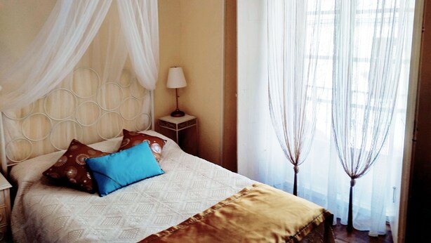 Un dormitorio con cama, mesita de noche, lámpara y cortinas translúcidas.