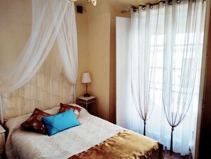 Un dormitorio con cama, mesita de noche, lámpara y cortinas translúcidas.
