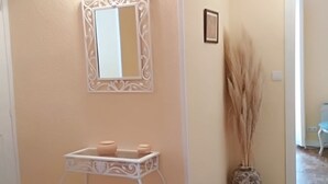 Una habitación con una consola blanca, un espejo y un florero con plantas secas.