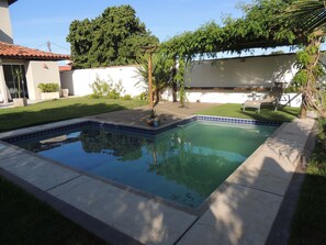 A rectangular swimming pool with blue tiles, surrounded by a concrete deck and a small grassy area. - Ótima Casa com Vista para a Praia de Manguinhos (Búzios)