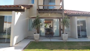 Een tweelaags huis met een overdekte veranda, grote ramen en potplanten.
