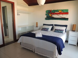 A bedroom with a bed, bedside tables, a nightstand, a wall art piece, and a door. - Ótima Casa com Vista para a Praia de Manguinhos (Búzios)