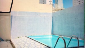 A swimming pool with a tiled deck, surrounded by a high wall and buildings in the background. - House nearby SEA with pool in Balneário Camboriú  (Pioneiros)