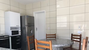 A compact kitchen with a refrigerator, microwave, stove, and wooden chairs around a granite table. - House nearby SEA with pool in Balneário Camboriú  (Pioneiros)