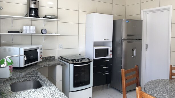 A compact kitchen with a gas stove, microwave, refrigerator, and a coffee maker on the countertop. - House nearby SEA with pool in Balneário Camboriú  (Pioneiros)