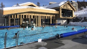 A pool area with multiple swimming pools, a bar area, and a building with large windows and wooden exterior.