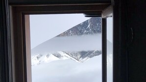 A window with a view of snow-covered mountains and a clear sky.