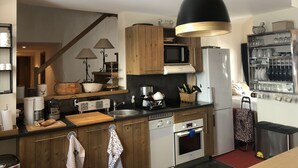 A modern kitchen with wooden cabinets, a microwave, a refrigerator, and a hanging pendant light.