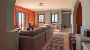 Una sala de estar moderna con un sofá grande, un comedor con mesa y sillas, y una cocina al fondo.