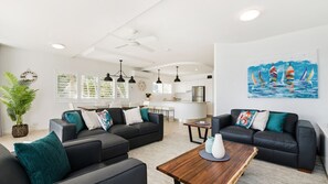 A modern living room with two black sofas, a wooden coffee table, and a kitchen in the background. - LOCATION DOESN'T GET ANY BETTER THAN THIS (Noosaville)