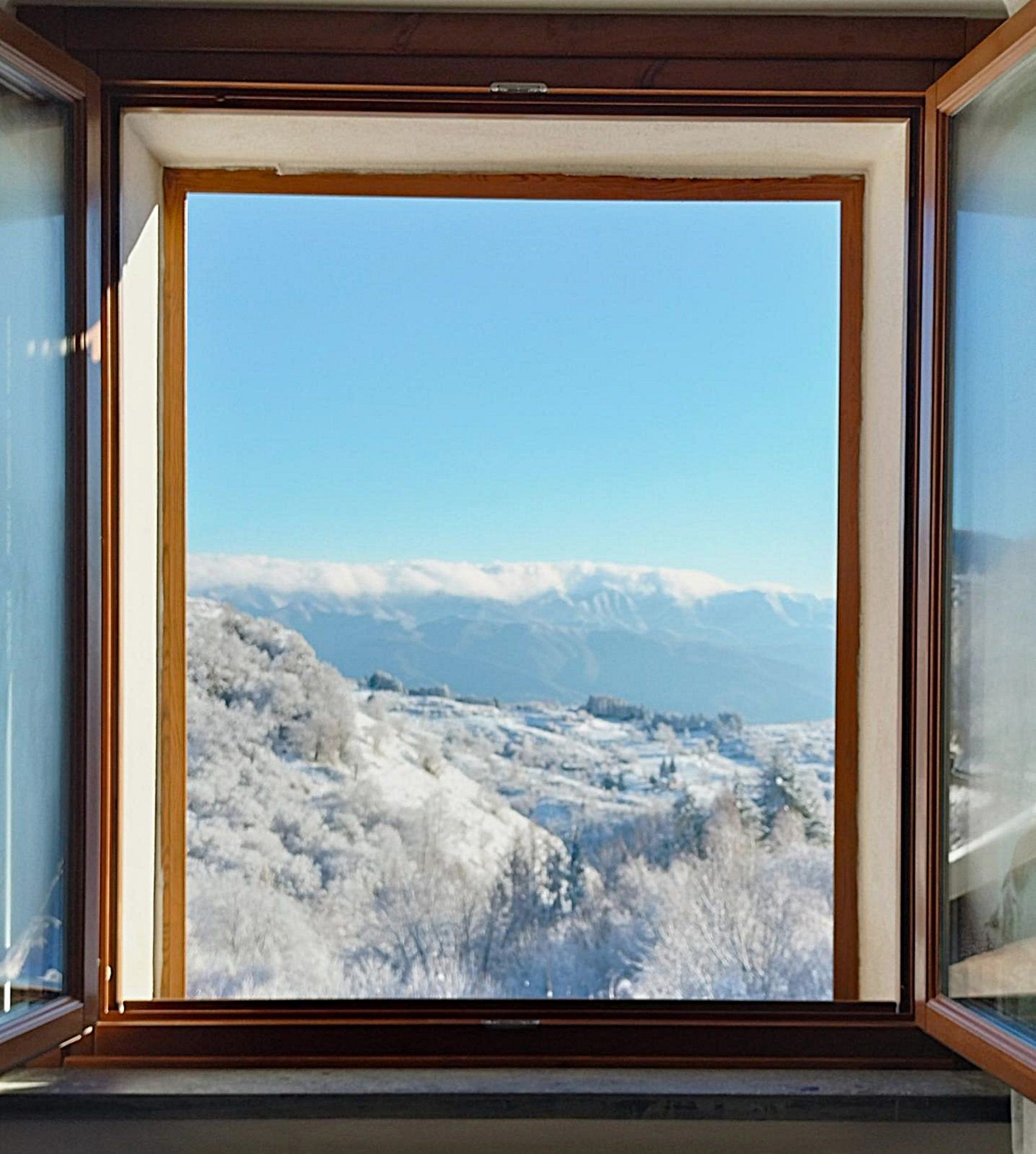 Ett fönster med utsikt över ett snöigt landskap och berg.