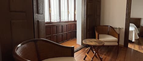 Une pièce avec un plancher en bois, une chaise en osier, une petite table ronde et un banc agrémenté de rideaux.