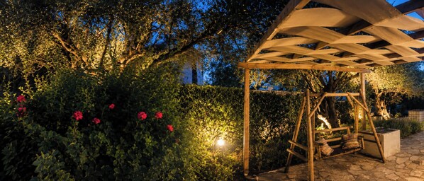 Ein Garten mit einer Pergola, umgeben von üppigem Grün und roten Blüten.